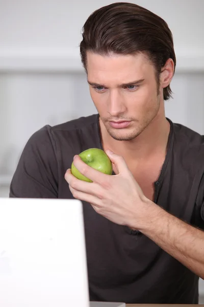 Ember eszik egy zöld almával, míg a laptop használatával — Stock Fotó