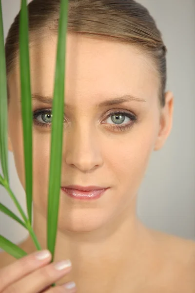 Ung kvinna med ett blad framför hennes ansikte — Stockfoto