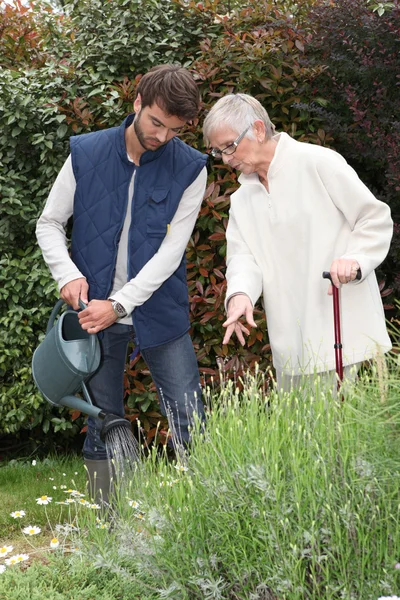 Ein Gärtner gießt Blumen in einem Garten und eine ältere Dame kommentiert — Stockfoto