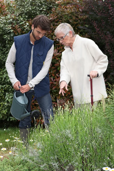 Молодой человек поливает растения с пожилой женщиной — стоковое фото
