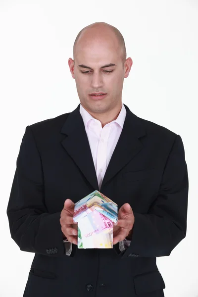 Un hombre de negocios sosteniendo una casa en miniatura hecha de billetes . —  Fotos de Stock