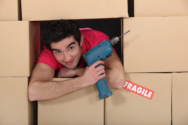 Um homem através de uma pilha de caixas de papelão com uma broca . — Fotografia de Stock