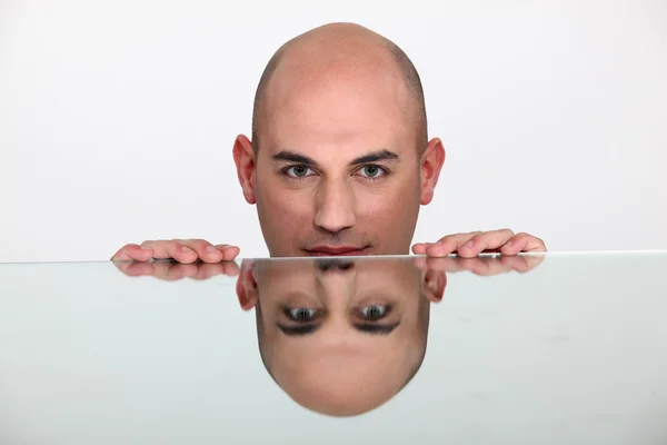 Schöner junger Mann mit reflektierendem Gesicht auf einem Glastisch — Stockfoto