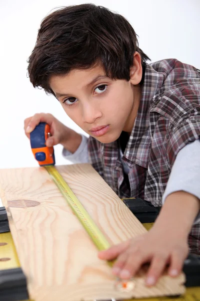 Молодий хлопчик вимірює дошку з дерева — стокове фото