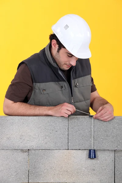 Un muratore che usa un filo a piombo per controllare il muro. . — Foto Stock