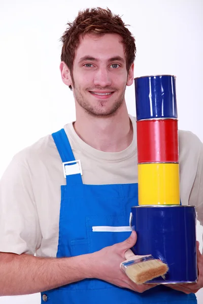 Young man in overalls with pots of paint in primary colors — Stock Photo, Image