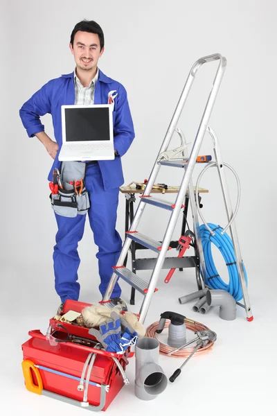 30-letni rzemieślnik pokazuje laptopa w pokoju pełnym narzędzi — Zdjęcie stockowe