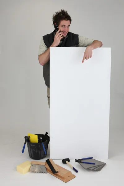 Tiler usando celular e apontando para cartaz — Fotografia de Stock