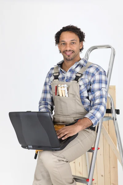 Tradesman leaning against a stepladder and using a laptop — Stock Photo, Image