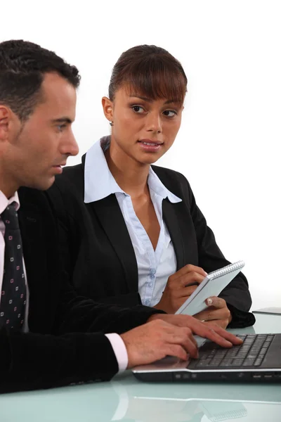 Woman taking notes as a businessman uses a computer — Stock Photo, Image