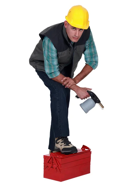 Tradesman posing with his foot propped on a toolbox and holding a spray gun — Stock Photo, Image