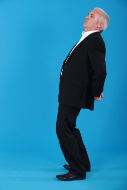Portrait of mature man standing back in profile against blue background clipart