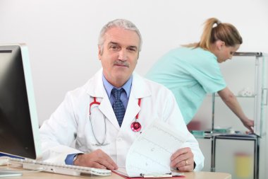 Senior doctor in his surgery with nurse in background clipart