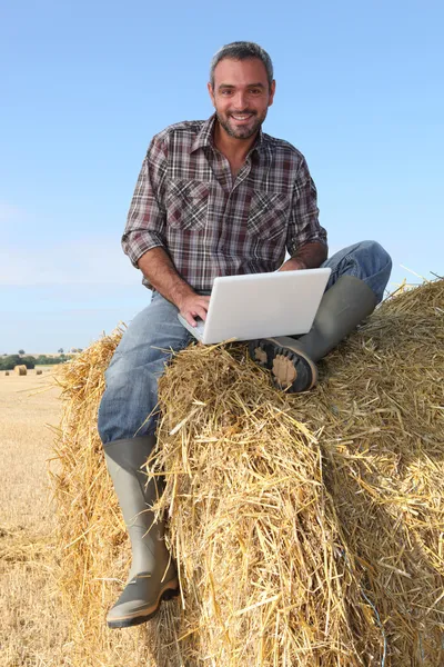 Farmer seated on straw bale and doing computer — Stock Photo, Image