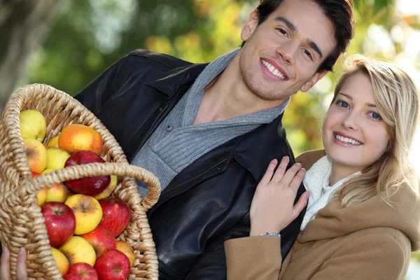 Jeune couple tout sourire avec panier plein de pommes — Photo