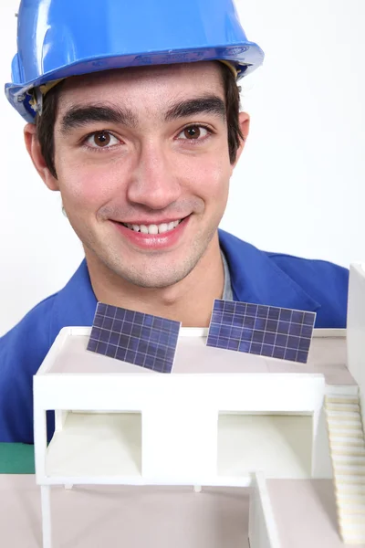 Jovem trabalhador com um modelo arquitetônico mostrando painéis solares — Fotografia de Stock