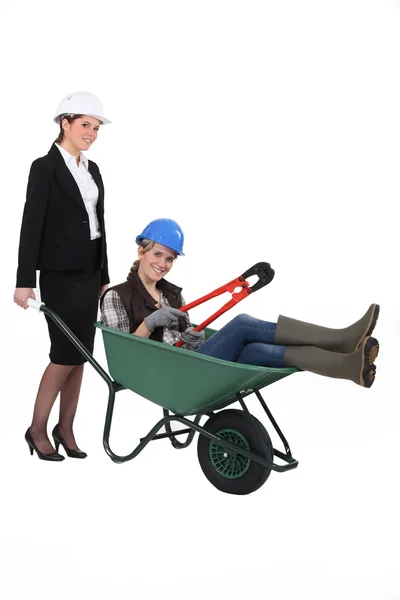 Uma mulher profissional empurrando um trabalhador de colarinho azul em um carrinho de mão — Fotografia de Stock