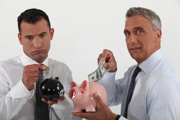 Two businessmen putting money in piggy-banks — Stock Photo, Image