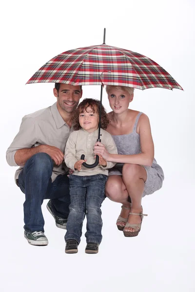 Young family crouching under an umbrella — Stock Photo, Image