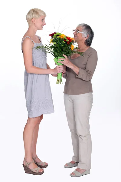 Ung kvinna ger en äldre dam blommor — Stockfoto