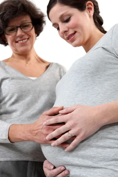 Jonge zwangere vrouw en moeder hand te leggen op haar buik — Stockfoto