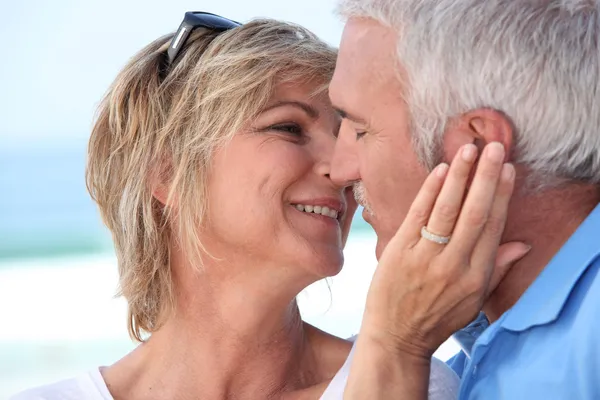 Medelålders par kysser på stranden. — Stockfoto