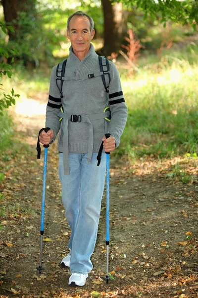 Старший джентльмен в лісі з прогулянковими полюсами — стокове фото