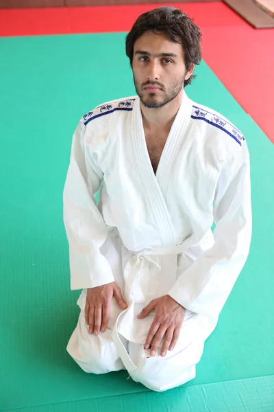 Volwassen mannetje geknield op mat in martial arts kleding — Stockfoto