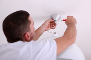 Man repairing ceiling light with screwdriver clipart