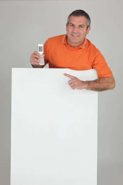 Mann hinter Mauer zeigt auf Handy — Stockfoto