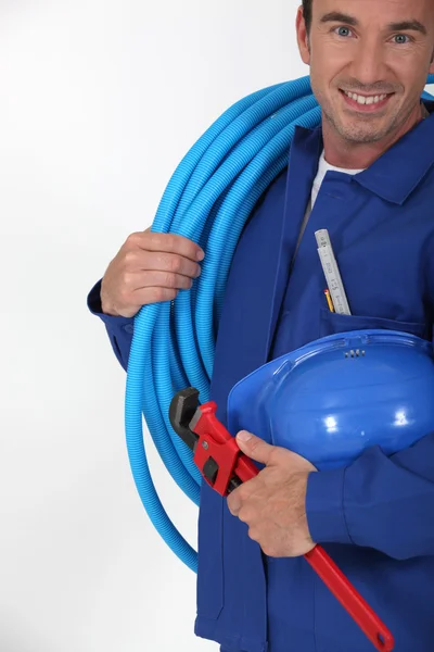 Чоловік тримає синю трубку, гайковий ключ і хардхат — стокове фото