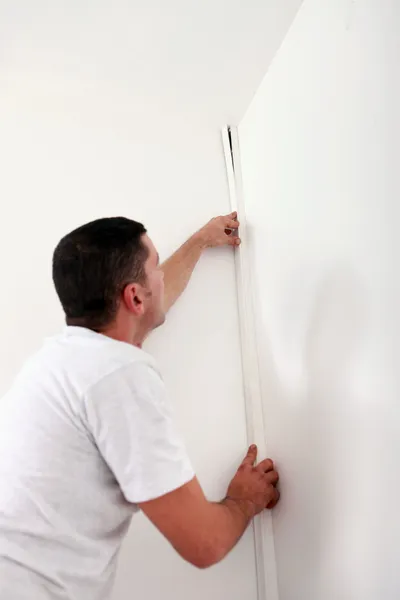 Handyman hiding a cable with a plinth — Stock Photo, Image