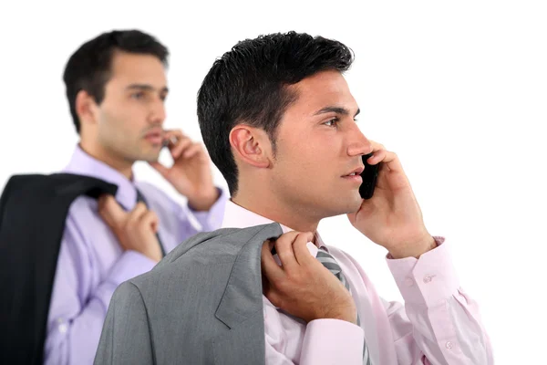 Два бизнесмена в куртках за плечами делают телефонные звонки — стоковое фото