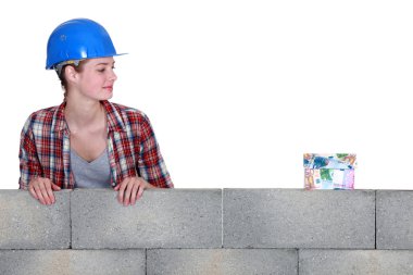 Female builder looking at a house made of money clipart