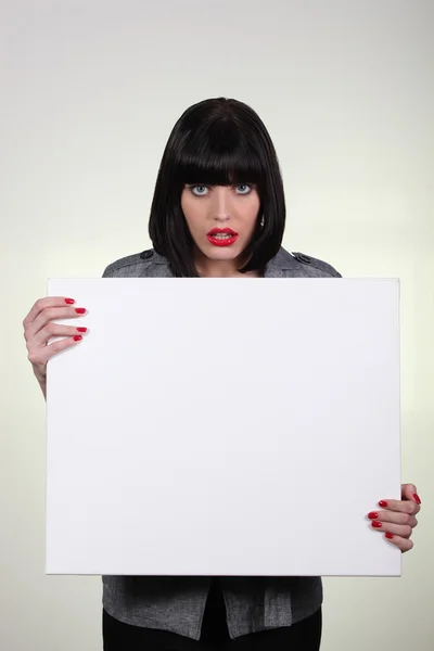 A woman looking amazed and showing a white panel — Stock Photo, Image