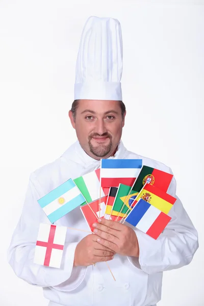 Um cozinheiro-chefe segurando muitas bandeiras estrangeiras — Fotografia de Stock