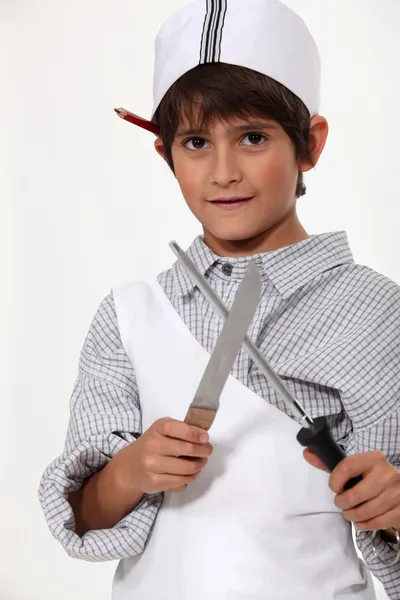 Мальчик, одетый как мясник, точит нож — стоковое фото