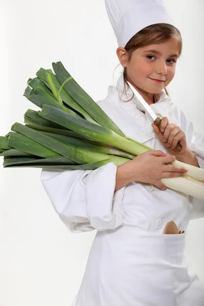 Little girl dressed as a chef holding bunches of leeks — Stock Photo, Image