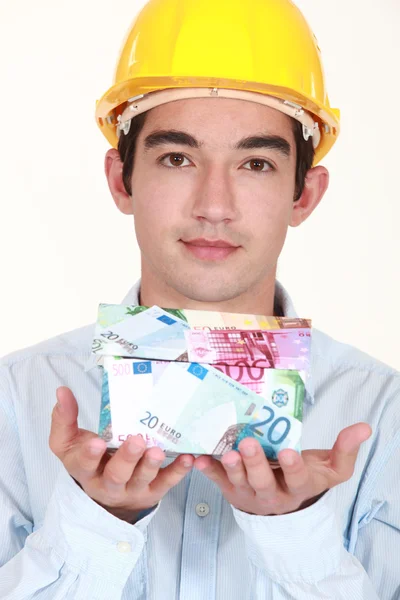 Young builder holding a house made of money — Stock Photo, Image