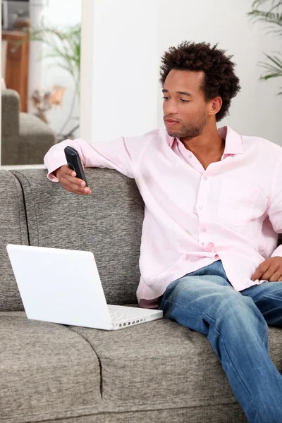 Hombre joven relajándose en el sofá y enviando mensajes de texto con su teléfono celular —  Fotos de Stock
