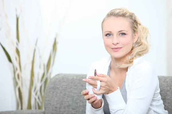 Een vrouw met een kopje koffie op haar bank. — Stockfoto