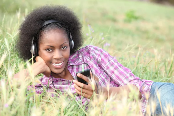 Uma mulher negra ouvindo música enquanto deitado na grama . — Fotografia de Stock