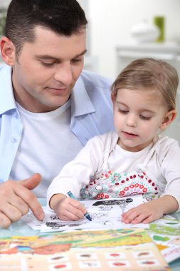 Little girl colouring under dad's watchful eye clipart