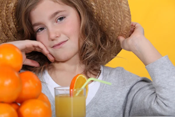 小女孩戴顶帽子喝杯橙汁 — 图库照片