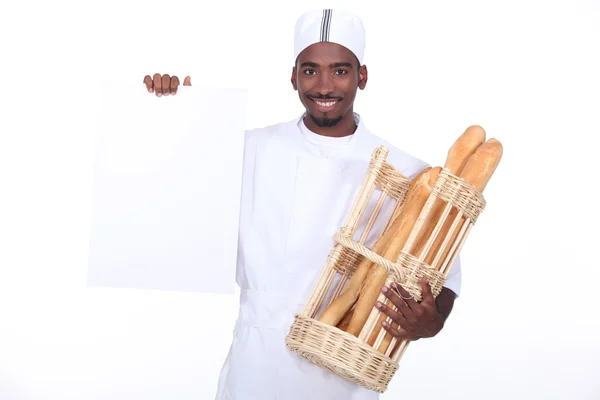 Panadero con una cesta de baguettes y una tabla en blanco para su mensaje —  Fotos de Stock