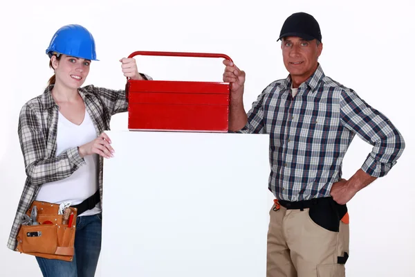 Comerciantes posando com sua caixa de ferramentas e um sinal em branco — Fotografia de Stock