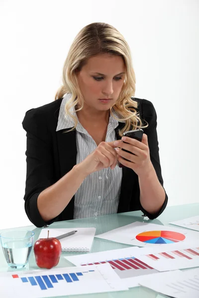 Eine Geschäftsfrau, die mit Diagrammen auf ihrem Schreibtisch SMS schreibt. — Stockfoto