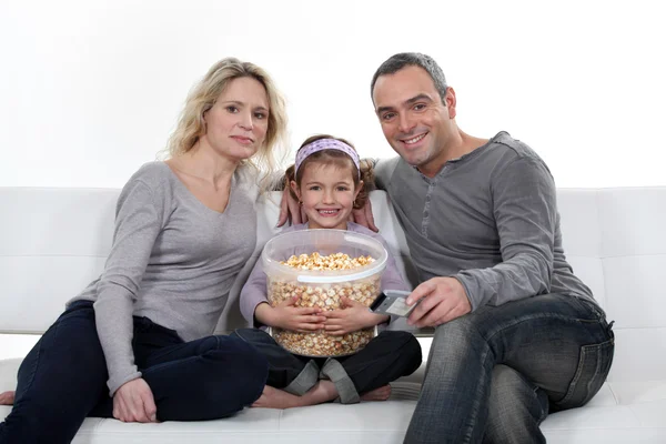 Family sitting on couch eating popcorn — Stock Photo, Image