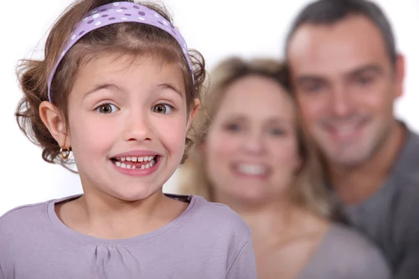 Roztomilá malá holčička se svými rodiči v pozadí. — Stock fotografie