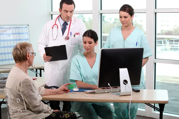 Doctor, patient, and medical secretaries at reception — Stock Photo, Image